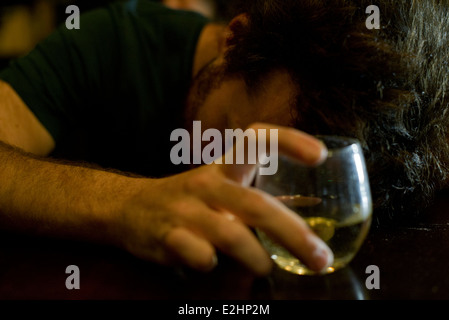 Uomo al bar con un bicchiere di whisky appoggiato la testa su bracci Foto Stock