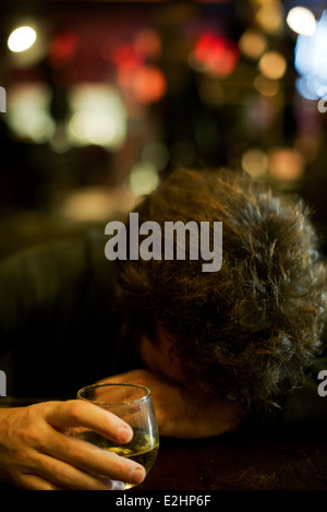 Uomo al bar con un bicchiere di whisky appoggiato la testa su bracci Foto Stock