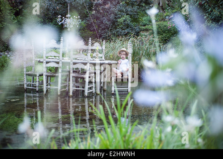 Little Boy seduti al tavolo da pranzo galleggiante sul lago Foto Stock