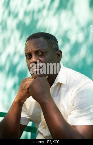 Ritratto di metà di età african american uomo con le mani sul mento, seduto in posizione di parcheggio e guardando la telecamera con espressione triste Foto Stock
