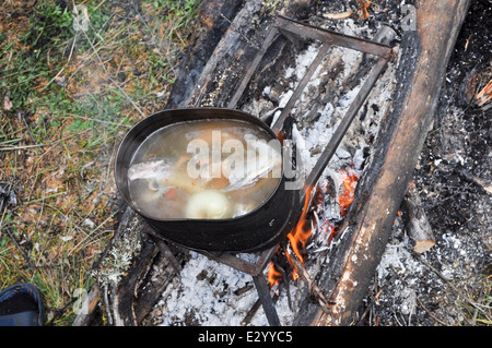 Pentola su un cavalletto in piedi sopra il fuoco. La preparazione di una zuppa di pesce sul fuoco durante il viaggio. Foto Stock