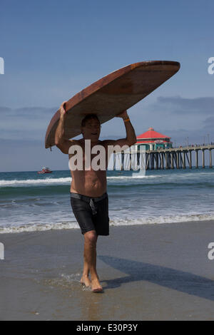 Un piccolo articolo di giornale al momento registrato che surfer George Freeth prima surfano Huntington Beach il 20 giugno 1914 . Oggi la città ha celebrato con i surfisti cavalcare schede boschive presso il molo.Bart Genovese porta il suo 13ft da 9 pollici con la tavola da surf in legno realizzato negli anni Trenta del Novecento dall'acqua Foto Stock