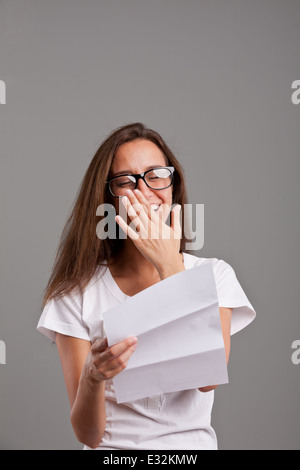 Un capelli lunghi brunette leggendo qualcosa si muove su un documento bianco o una lettera e ridere o sorridere Foto Stock
