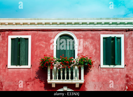 Verde finestre veneziane con fiori. Parete rossa Foto Stock