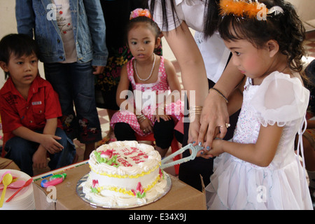 Un insegnante è aiutare un bambino di 6 anni ragazza asiatica tagliare la sua torta di compleanno presso la Scuola di Angkor in Kampong Cham, Cambogia. Foto Stock