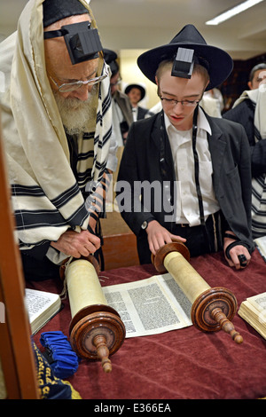 Un giovane ragazzo lettura da un rotolo di Torah al mattino servizi in sede Lubavitch in Crown Heights, Brooklyn, New York. Foto Stock