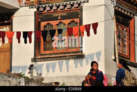 Due studentesse seduto da casa tradizionale con la linea di essiccazione di lana, Trashigang, Est Bhutan Foto Stock