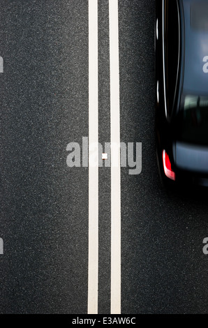 Doppia bianca divisore di linee su asfalto con il passaggio di un auto Foto Stock