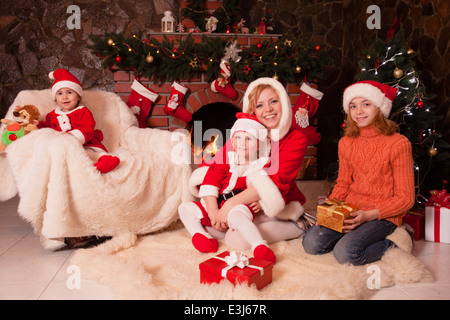 Madre e bambini sono seduti vicino al camino e l albero di natale con confezioni regalo. Fratello e Sorella di santa adatta Foto Stock