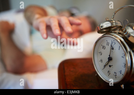 Matura in letto con uomo di raggiungere per spegnere la sveglia Foto Stock