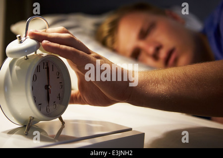 Ragazzo adolescente svegliarsi a letto e spegnere la sveglia Foto Stock