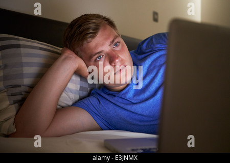 Ragazzo adolescente utilizzando laptop in letto a notte Foto Stock