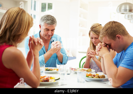 Famiglia dicendo la preghiera prima di mangiare pasti a casa insieme Foto Stock