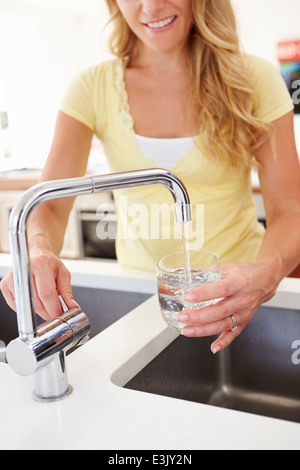 Donna versando un bicchiere di acqua dal rubinetto in cucina Foto Stock