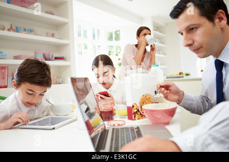 Famiglia utilizzando dispositivi digitali a tavolo per la colazione Foto Stock