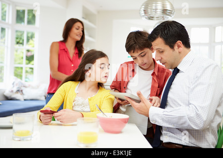 Famiglia utilizzando dispositivi digitali a tavolo per la colazione Foto Stock