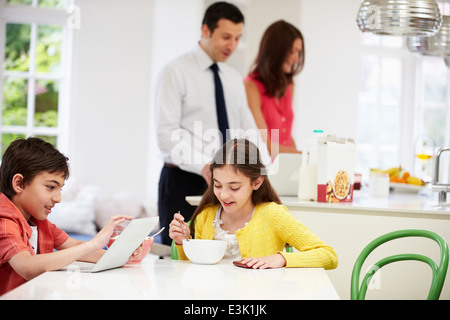 Famiglia utilizzando dispositivi digitali a tavolo per la colazione Foto Stock