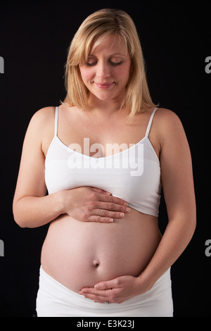Ritratto Di Donna Incinta indossando bianco su sfondo nero Foto Stock