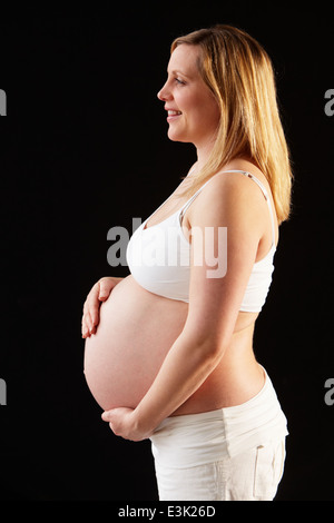 Ritratto Di Donna Incinta indossando bianco su sfondo nero Foto Stock