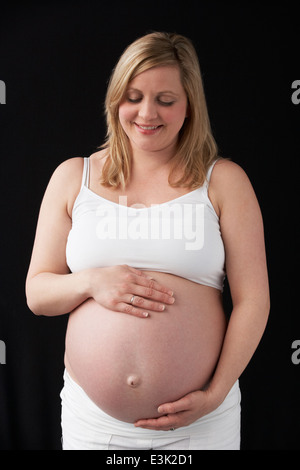 Ritratto Di Donna Incinta indossando bianco su sfondo nero Foto Stock