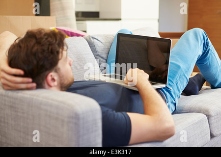 L'uomo rilassante sul divano con il computer portatile nella nuova casa Foto Stock