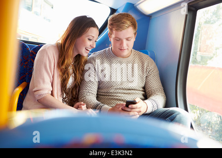 Un adolescente matura la lettura di un messaggio di testo sul bus Foto Stock