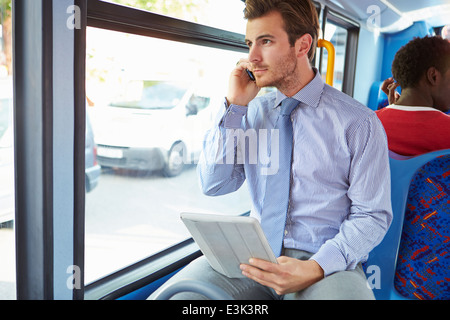 Imprenditore utilizzando il telefono cellulare e la tavoletta digitale sul bus Foto Stock