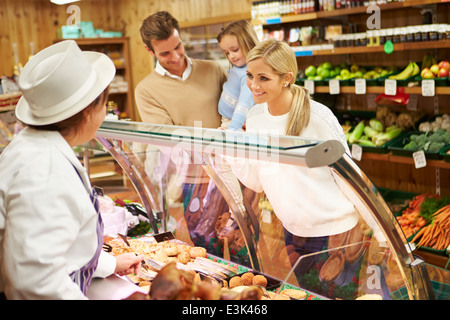 Femmina assistente di vendita di servire la famiglia in negozio di specialità gastronomiche Foto Stock