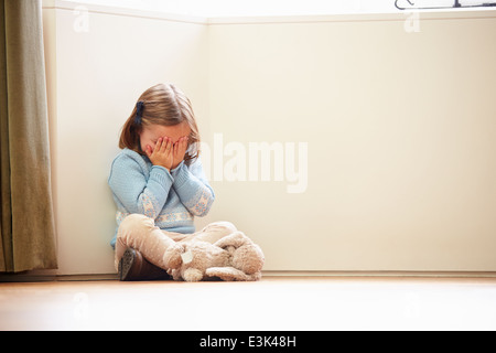 Infelice bambino seduto sul pavimento in un angolo a casa Foto Stock