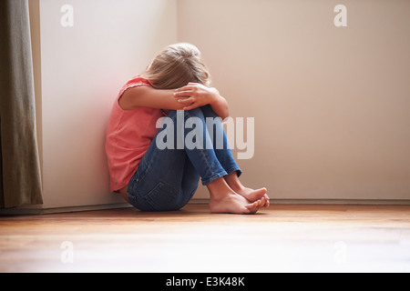 Infelice bambino seduto sul pavimento in un angolo a casa Foto Stock