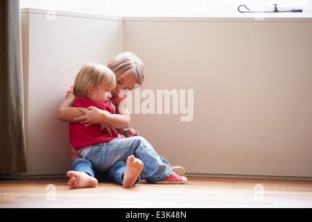 Infelici bambini seduti sul pavimento in un angolo a casa Foto Stock