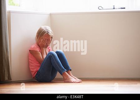 Infelice bambino seduto sul pavimento in un angolo a casa Foto Stock