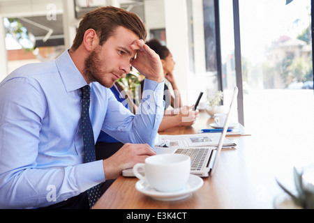 Sottolineato uomo d affari con computer portatile in Coffee Shop Foto Stock