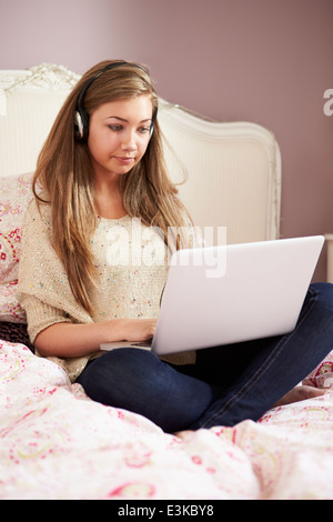 Ragazza adolescente sdraiato sul letto tramite computer portatile che indossano le cuffie Foto Stock