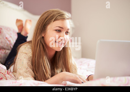 Ragazza adolescente sdraiato sul letto tramite computer portatile Foto Stock