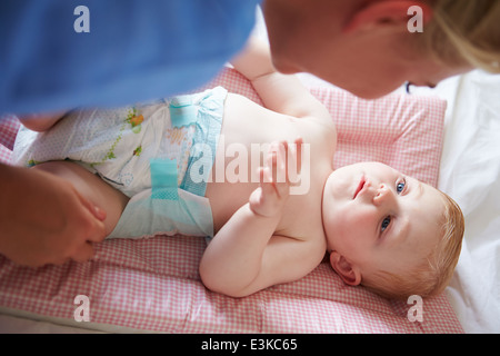 Madre modifica Baby figlio il pannolino come egli giace sul tappetino Foto Stock