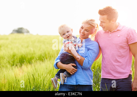 Famiglia passeggiate nel campo portando giovane figlio bambino Foto Stock