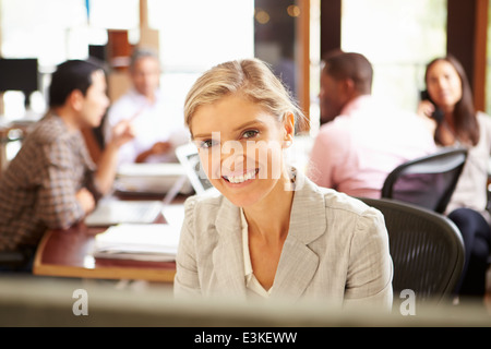 Imprenditrice lavorare alla scrivania con sale riunioni in background Foto Stock