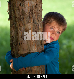 Little Boy abbracciando un albero in un parco Foto Stock