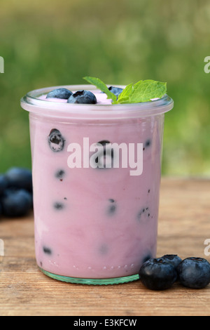 Mirtillo yogurt in un recipiente su un tavolo in legno servito con mirtilli freschi Foto Stock