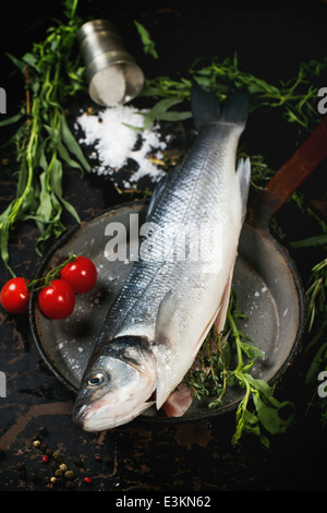 Pesce crudo spigola servito con erbe aromatiche, sale marino e i pomodori ciliegia su vintage pan su tavoli in legno nero Foto Stock