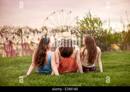 Vista posteriore di tre giovani donne (18-19) seduto sull'erba Foto Stock