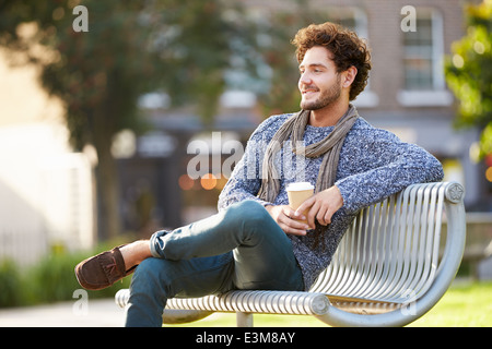 Uomo relax su una panchina nel parco con caffè da asporto Foto Stock