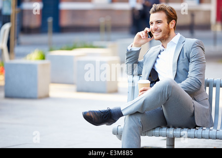 Imprenditore su una panchina nel parco con caffè utilizzando il telefono cellulare Foto Stock