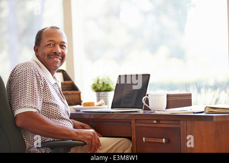 Senior uomo utilizzando laptop sulla scrivania a casa Foto Stock
