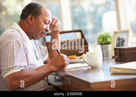 Uomo Senior iscritto nelle sue memorie nel libro seduti alla scrivania Foto Stock