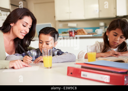 Madre aiutando i bambini con i compiti a tavola Foto Stock