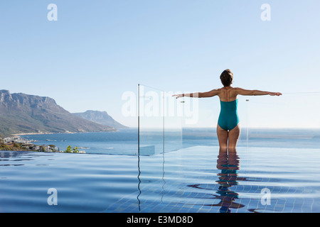 Donna crogiolarsi nella piscina a sfioro con vista sull'oceano Foto Stock