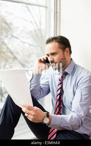 Grave adulto medio imprenditore documento di lettura mentre su chiamata in ufficio Foto Stock