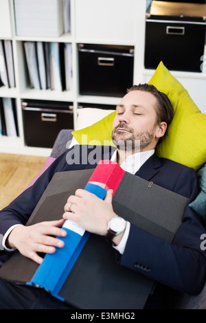 Adulto medio imprenditore con cartella che dorme sul divano nell'ufficio Foto Stock